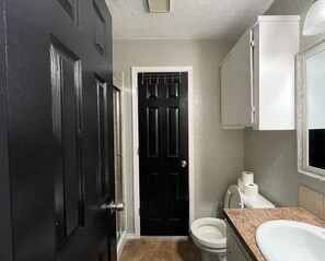 Une salle de bain avec une porte noire, des toilettes blanches et un lavabo doté d’un plan de toilette beige.
