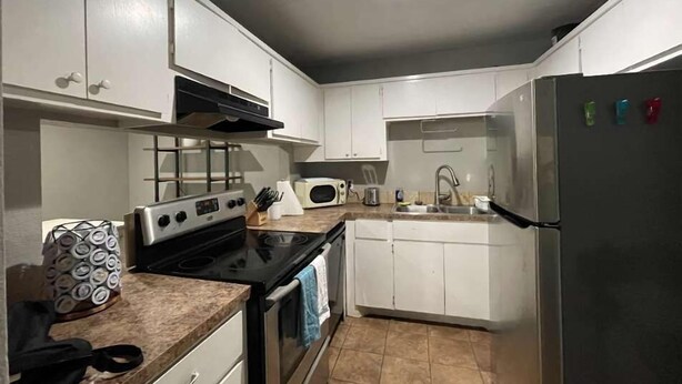 Una cocina moderna con armarios blancos, un refrigerador de acero inoxidable, un microondas y una estufa.