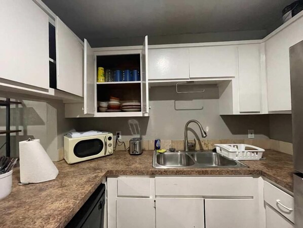 Una cocina compacta con armarios blancos, un microondas, un fregadero y un escurreplatos.