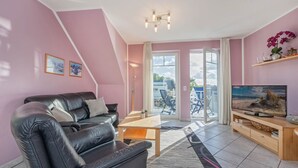Un salon moderne avec un canapé en cuir noir, une table basse en bois, un téléviseur à écran plat et une grande fenêtre donnant sur l’extérieur.
