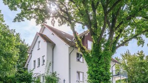 Un bâtiment blanc à deux étages, doté d’un toit en pente, entouré d’une végétation luxuriante et d’arbres.