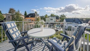 Une terrasse avec une table ronde et deux chaises, donnant sur un quartier résidentiel avec des maisons et des arbres.