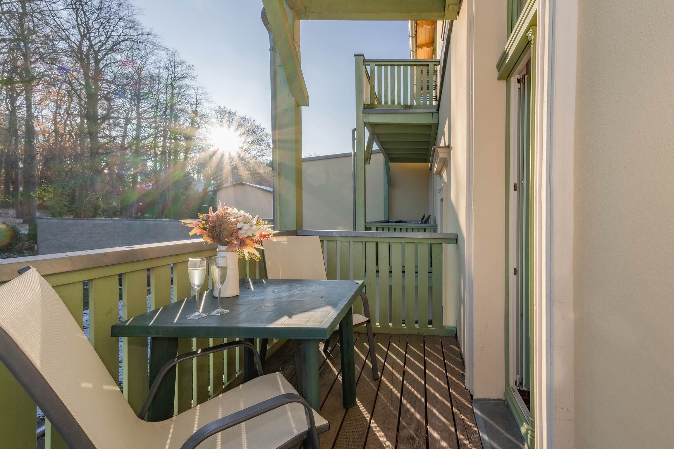 A balcony with a table set for two, a chair, and a vase with flowers.