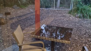 A stone bench with a metal frame, a metal table with a reflective surface, and a metal chair.