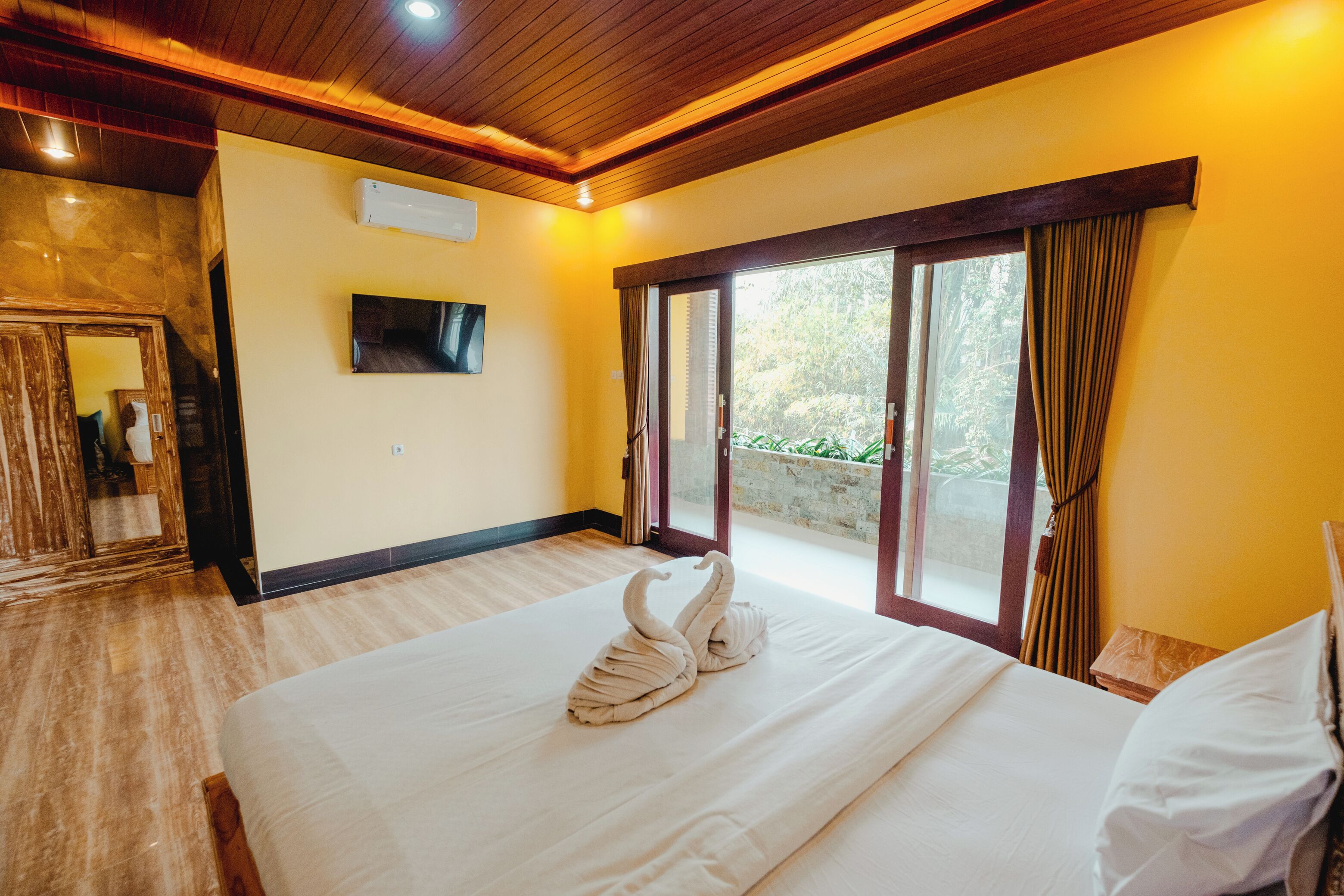 A hotel room with a large bed, a flat-screen TV, and a sliding glass door leading to a balcony.