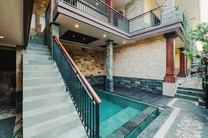 A multi-level interior with a central staircase, stone walls, and a small pool area. - Tutde Guest House  (Abiansemal)
