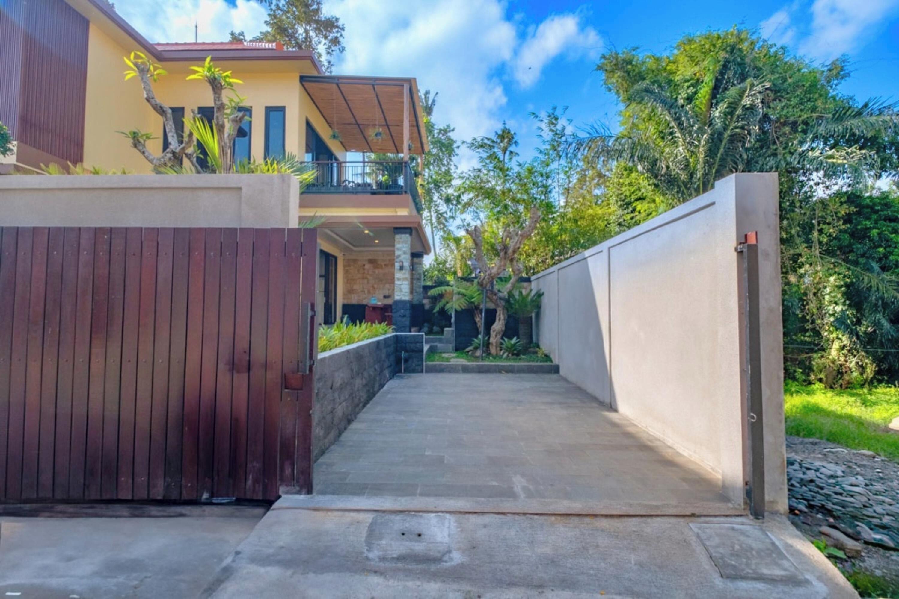 A modern house with a concrete pathway leading to the entrance, surrounded by greenery and a wooden fence.