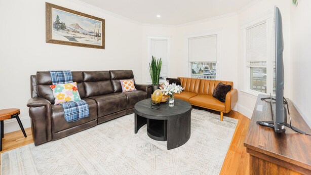 A living room with a brown leather sofa, a black coffee table, and a television on a wooden stand. - Stylish 4 Bedroom Townhouse in Boston, Walkable to Train, Quiet & Safe Area 76 (Boston)