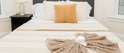 Una cama bien hecha con un edredón a rayas, una manta marrón y una almohada blanca.