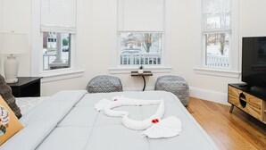 A hotel room with a bed, two patterned chairs, a small table with a plant, a TV, and a window with a view of a snowy street. - Stylish 4 Bedroom Townhouse in Boston, Walkable to Train, Quiet & Safe Area 76 (Boston)