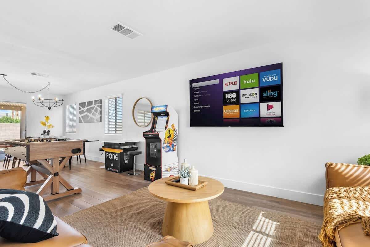 Un salon moderne doté d’un téléviseur à écran plat diffusant des services de streaming, d’une table de baby-foot et d’un coin salon confortable.
