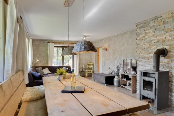 A modern living room with a wooden dining table, a sofa, a fireplace, and a stone wall. - Chalet Leogang Near Skilift & Bikepark (Leogang)