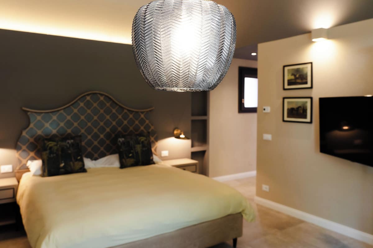 Quarto com cama, mesas de cabeceira, TV fixada na parede e luminária pendente.