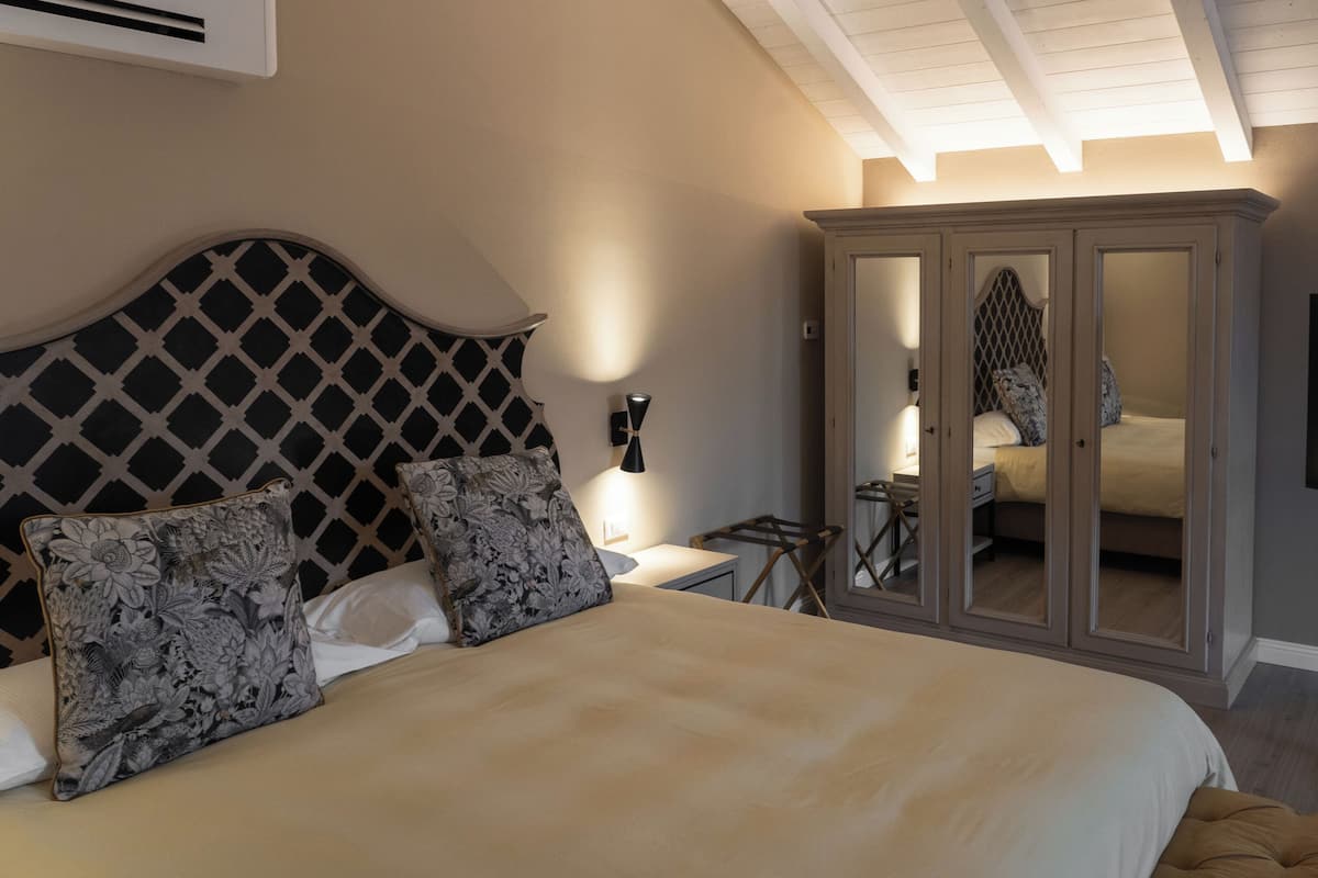 Quarto com cama, guarda-roupa, mesa de cabeceira, abajur e televisão.