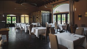 Un restaurant doté de nombreuses tables et chaises, de grandes fenêtres et d’un mur orné de motifs.