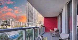 A balcony with a city view, a red wall, and a table with chairs.