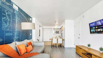 Ein modernes Wohnzimmer mit einer großen Karte an der Wand, einem Sofa mit orangen Kissen, einem Essbereich und einem Fernseher, der einen Film zeigt.