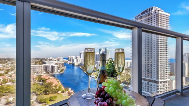 Un balcon avec deux coupes à champagne, une bouteille et une planche en bois sur laquelle sont disposés des raisins.