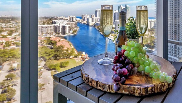 A balcony with two champagne flutes, a bottle, and a wooden board with grapes.
