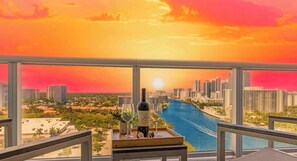 A balcony with a city view, a table with a bottle of wine, and two glasses.