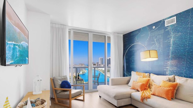 A modern living room with a large window, a flat-screen TV, a sofa with orange pillows, and a map-themed wall. - Modern 2BR 2BA Oasis & pool (Hallandale Beach)