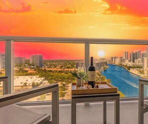Un balcón con vistas a la ciudad, una mesa con una botella de vino y dos copas.