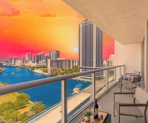 A balcony with a cityscape view, a railing, and a table with a bottle and glass.