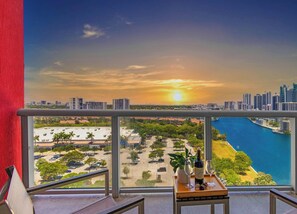 A balcony with a city view at sunset, a bottle of wine, and a glass on a tray.