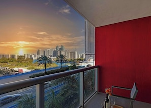 A balcony with a red wall, a view of a city skyline, and a road with palm trees.