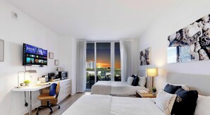 Habitación de hotel con cama, escritorio, televisor y vista al atardecer.