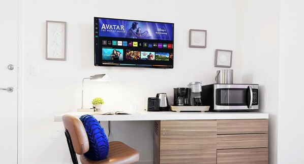 Un espace de bureau moderne comprenant un bureau, une chaise, une machine à café, un four à micro-ondes et un téléviseur affichant l’interface d’un service de diffusion en continu.