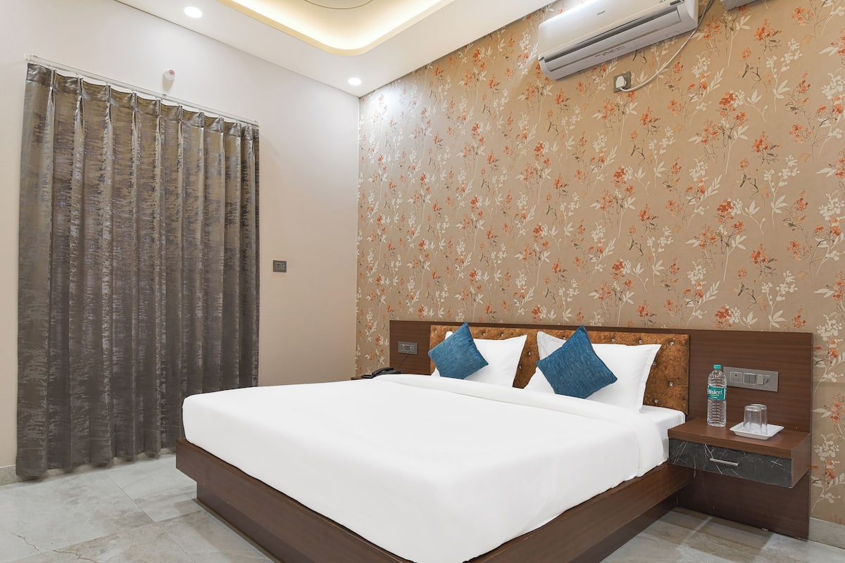 A hotel room with a large bed, a nightstand, a water bottle, and a thermostat on the wall.