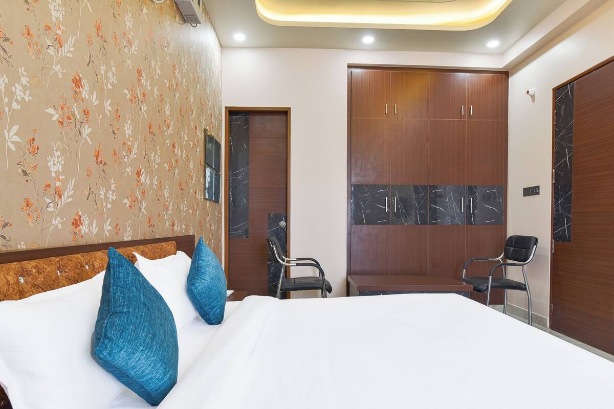 A hotel room with a large bed, two chairs, a wardrobe, and a floral wallpaper design.