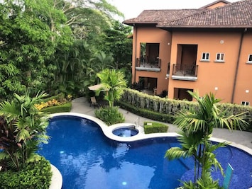 From the room above, the pool is visible as a sparkling centerpiece surrounded by lush greenery