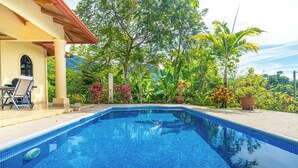 A swimming pool with tiled blue edges, surrounded by lush greenery and a patio area with a chair and table. - Gated Community-Privacy, Ocean Views-pool-Ojochal-sleep 9 (Ojochal)