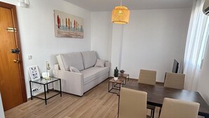 A modern living room with a white sofa, a dining table with chairs, a small side table, and a hanging light fixture. - Your Sanctuary with a View of History: Live Córdoba from the Heart of the City (Córdoba)