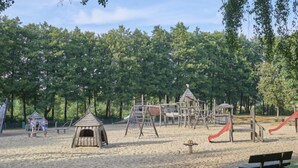 Un’area giochi con diverse strutture, tra cui scivoli e giochi di arrampicata, circondata da alberi.