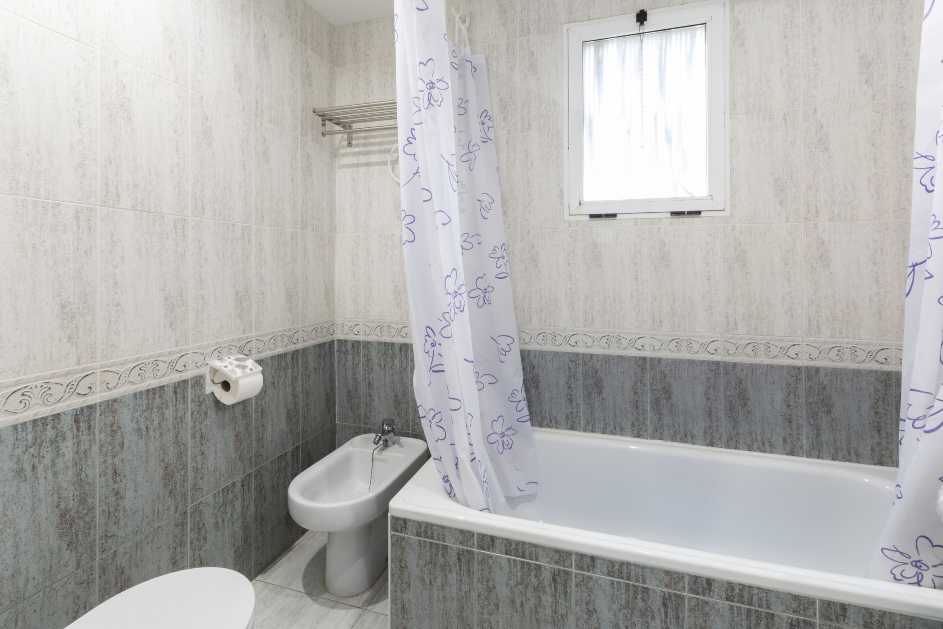 A bathroom with a bathtub, bidet, toilet, and a window with a curtain.