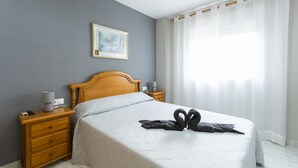 A neatly made bed with a quilted white cover, a wooden headboard, and a bedside table with a lamp. - Estornell With 2 Bedrooms and 1 Bathrooms (Daimuz)