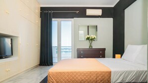 Habitación de hotel con cama, televisor, cómoda, espejo y vistas al exterior.