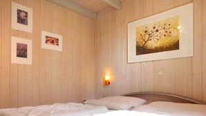 A room with wooden walls, a bed with white bedding, and three framed pictures on the wall. - Ferienhaus im Skandinavischen Stil (Mirow)