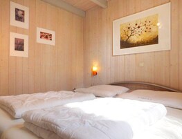 Une pièce aux murs en bois, un lit avec une literie blanche et trois tableaux encadrés accrochés au mur.
