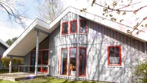 A modern house with a sloped roof, large windows with red frames, and a visible porch area. - Ferienhaus im Skandinavischen Stil (Mirow)