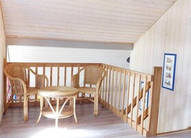 Une pièce avec un plafond en bois, un balcon doté d’une balustrade en bois et des meubles en osier, notamment des chaises et une table.
