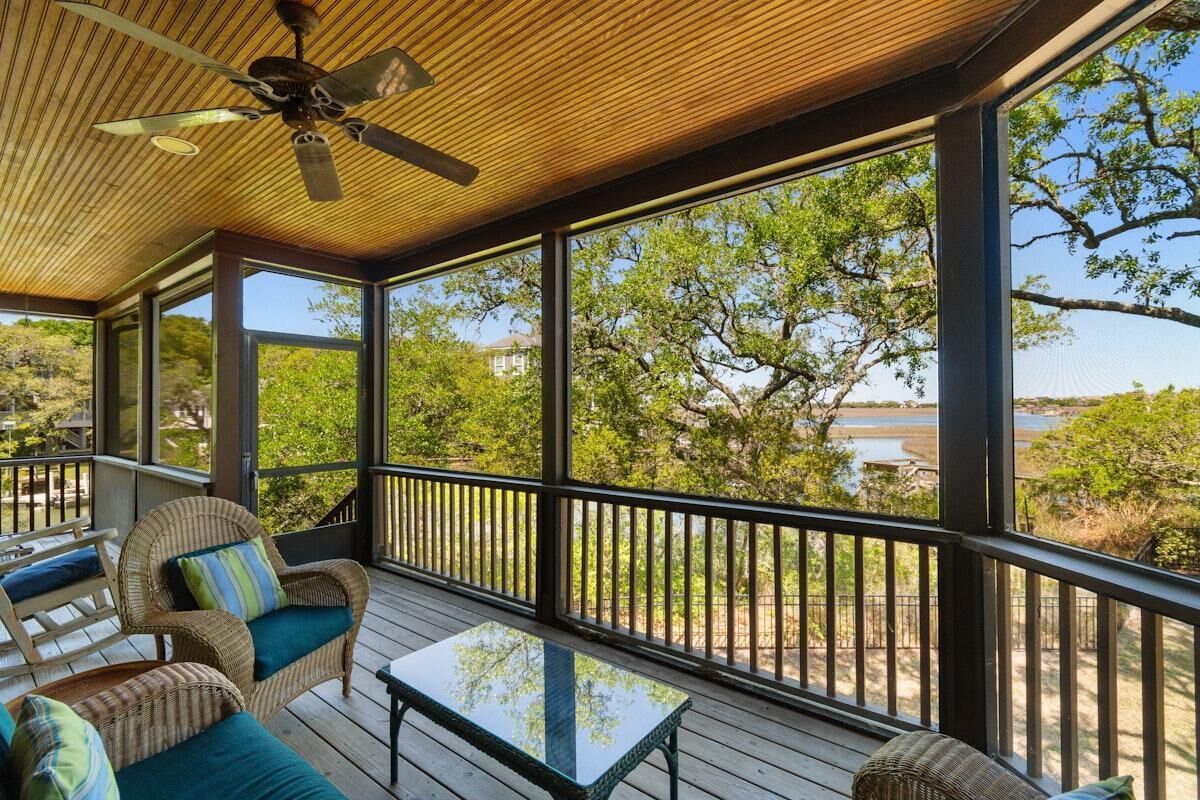 Une terrasse extérieure aménagée avec des meubles en osier, un ventilateur de plafond et une vue sur les arbres et l’eau.
