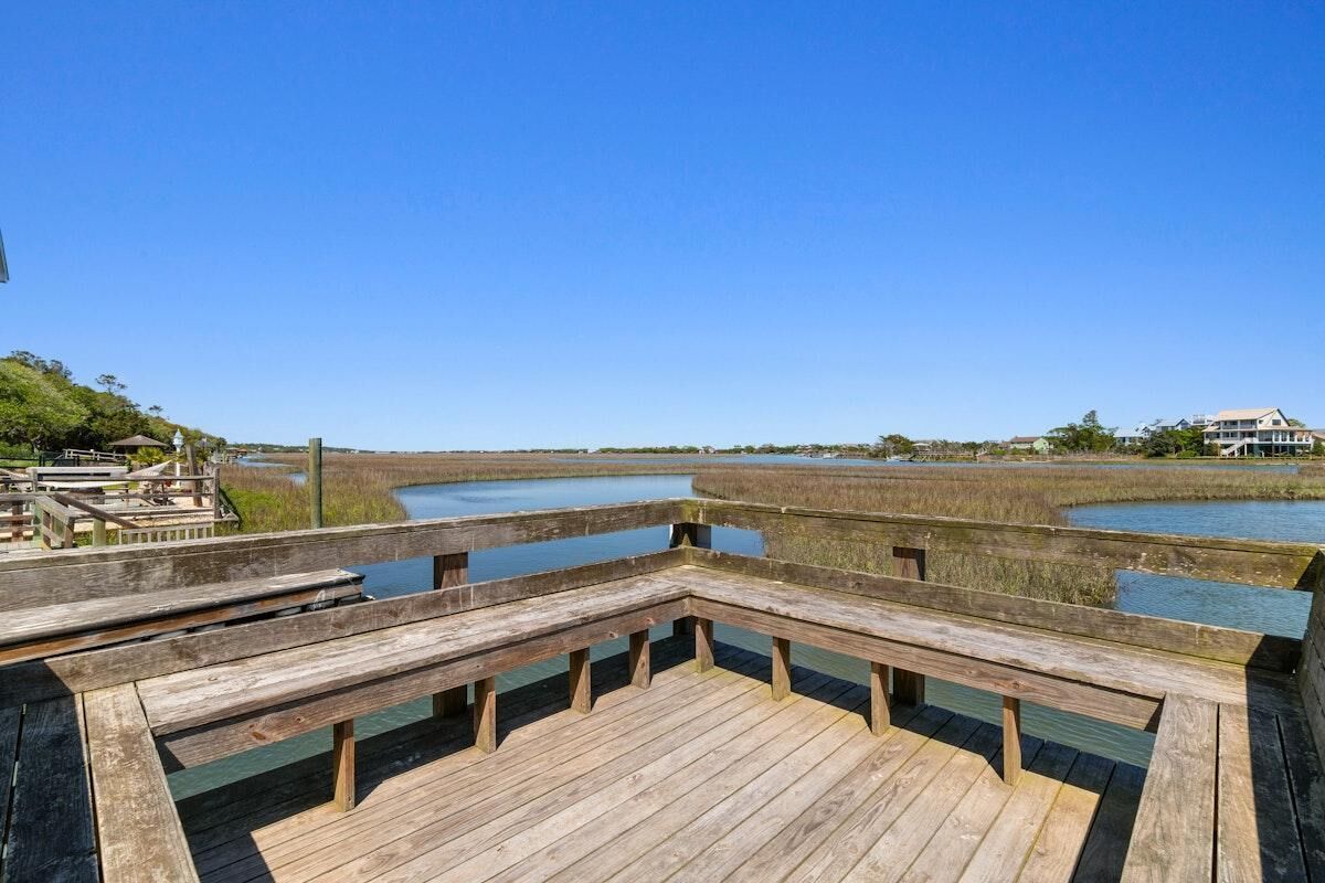A wooden deck with benches overlooking a marshy landscape with water and buildings in the distance.