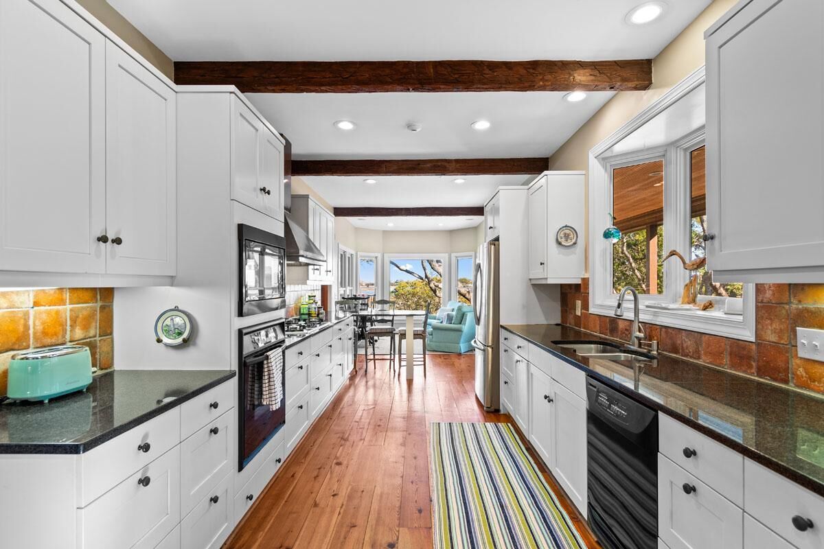 A modern kitchen with white cabinets, a wooden floor, and a striped rug.