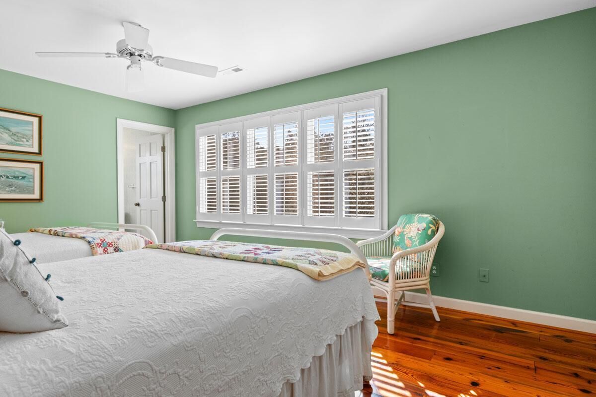 A bedroom with two beds, a white ceiling fan, a window with shutters, and a green wall.