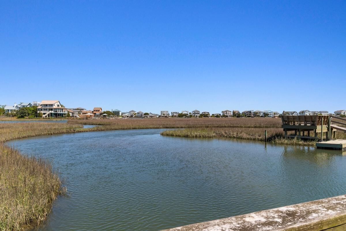 A calm water body with a wooden dock and a bench, surrounded by residential buildings and marshland.