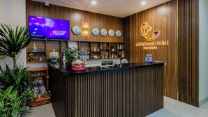 A hotel reception desk with a wooden finish, a TV mounted on the wall, and a neon sign for the Abasand Hotel. - Alba Sand Hotel Phu Quoc (Phu Quoc)